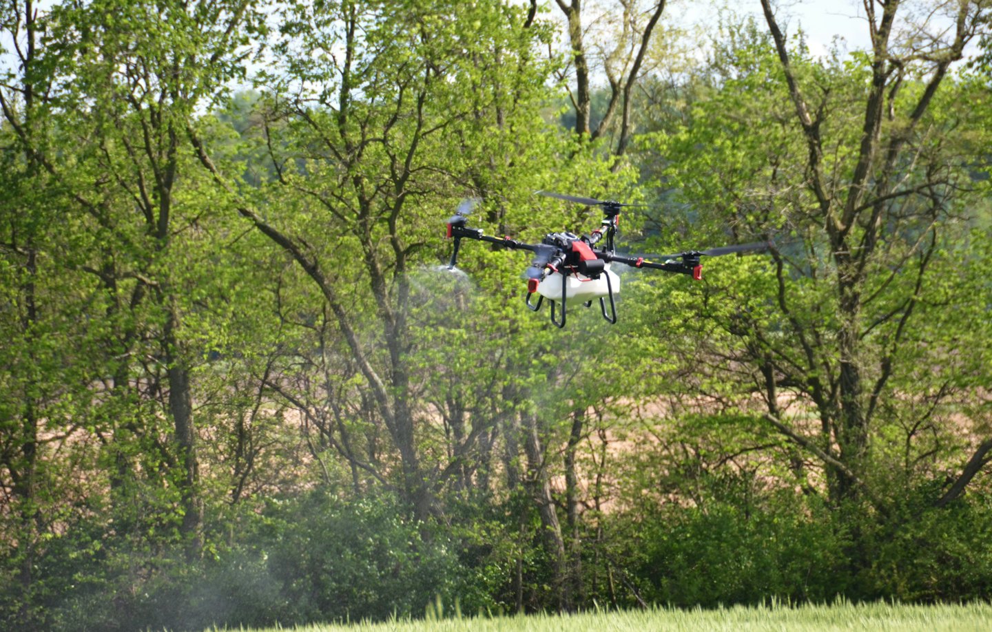 Un drone agricole pulvérise de la brume sur un champ de cultures vertes.